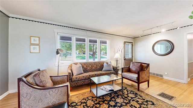 Living room with patterned seating, a glass coffee table, floral rug, and large windows.