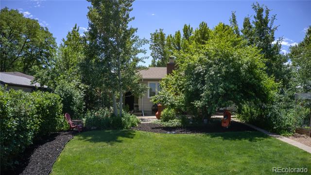 Home’s backyard with a broad lawn, mature trees, landscaped beds, and patio seating.