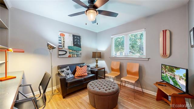 Furnished den with a leather sofa, orange chairs, tufted ottoman, and ceiling fan.