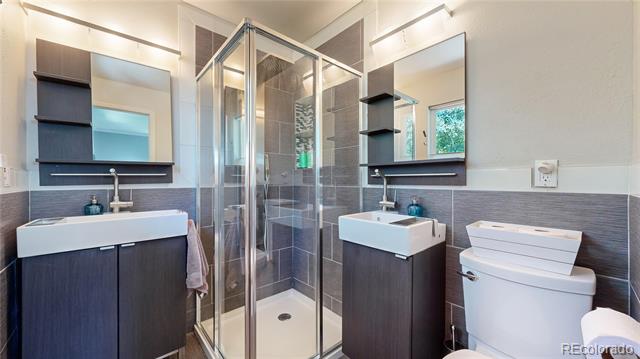 Modern bathroom with a glass shower, dark vanities, white sinks, and a toilet.