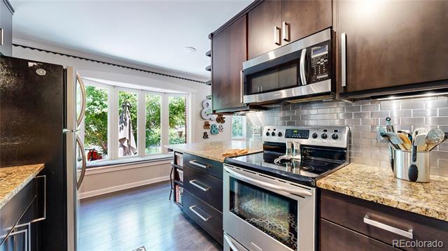 Kitchen with dark wood cabinets, granite countertops, stainless steel appliances, and large windows.