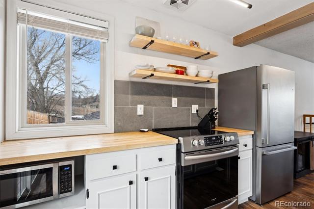 Kitchen with white cabinets, wood countertops, open shelves, and stainless steel appliances.