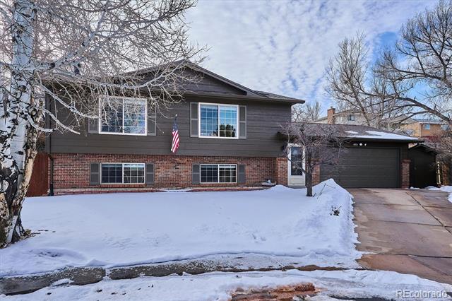 Split-level home with dark siding, brick facade, attached garage, and snow-covered front yard.