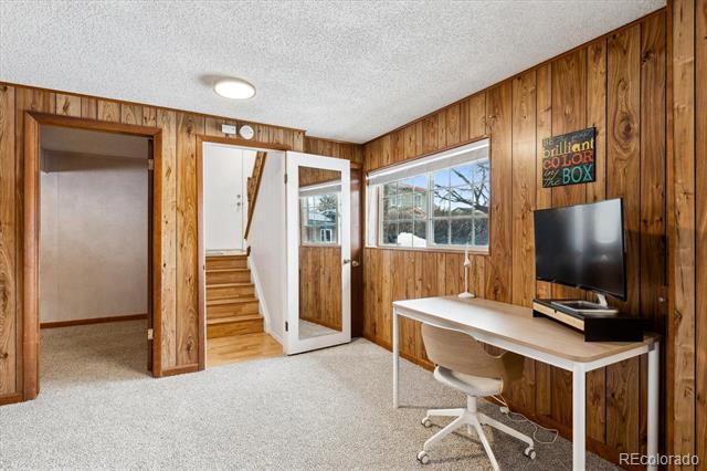 Home office with wood-paneled walls, a white desk, television, and staircase doorway.