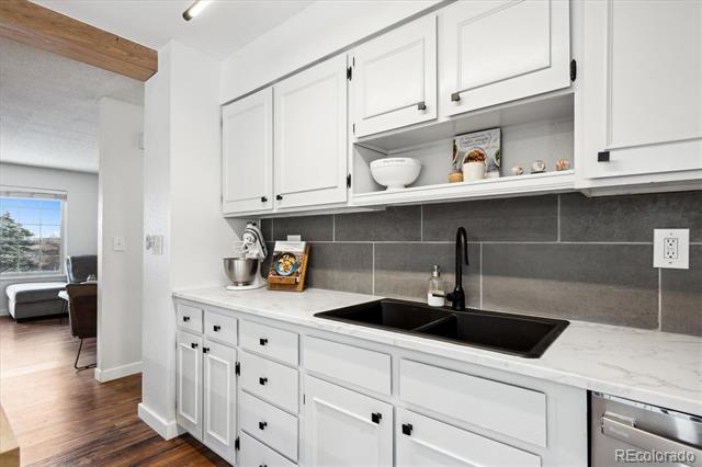 Kitchen with white shaker cabinets, gray tile backsplash, and a black sink beneath an open display shelf.