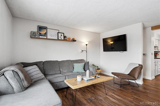 Living room with a gray sectional, wood floors, wall-mounted TV, and brown leather lounge chair.