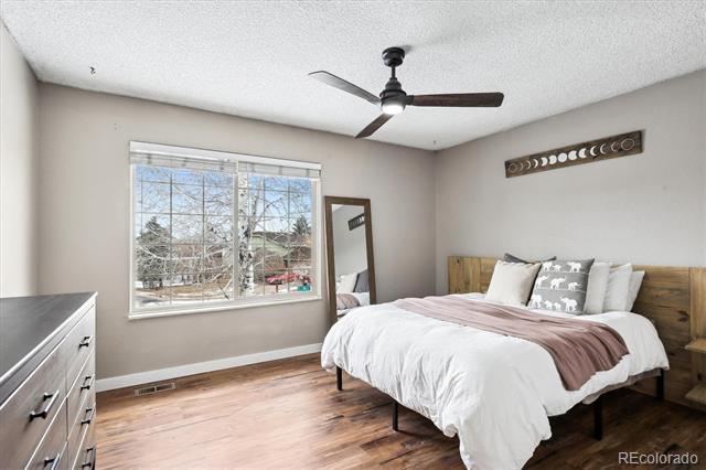 Furnished bedroom with a white bed, wood headboard, ceiling fan, and large window.