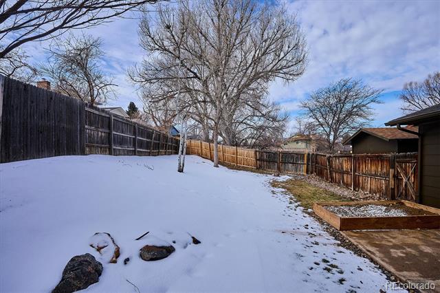 Snow-covered backyard with leafless trees, a wooden privacy fence, and a raised garden bed.