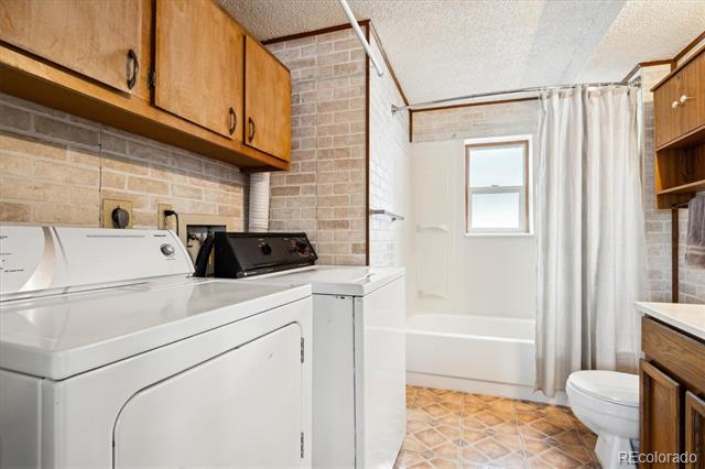 Bathroom and laundry room with a washer and dryer beside a curtained bathtub.