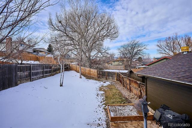 Snow-covered fenced backyard with a leafless tree, raised garden bed, and detached garage.