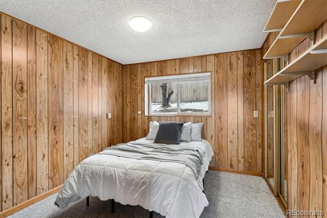 Bedroom with wood-paneled walls, white bedding, and built-in shelves beside a window overlooking snow.