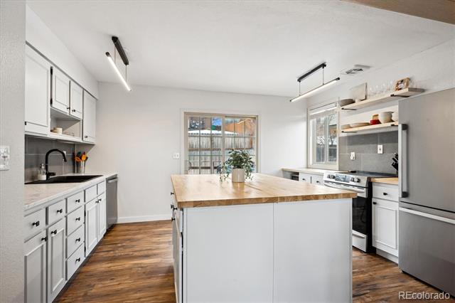 Bright white kitchen with a butcher-block island, stainless appliances, and warm wood floors.