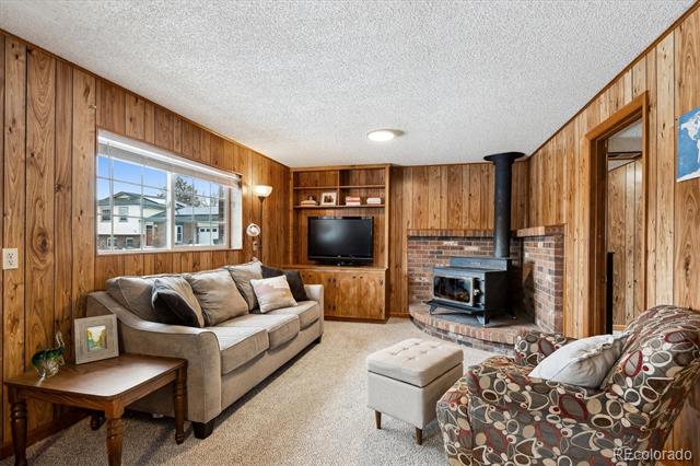 Wood-paneled living room with a brick fireplace, wood stove, and sofas.