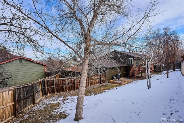 Home’s rear exterior with a raised deck and stairs beside a snow-covered yard and leafless trees.