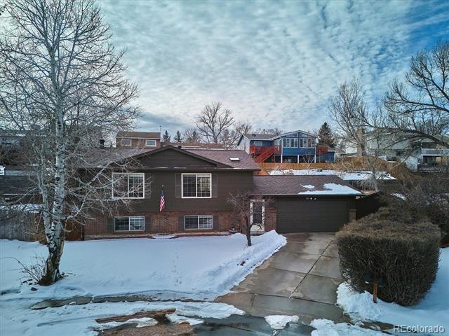 Brown two-story house with an attached garage, snowy lawn, and concrete driveway.