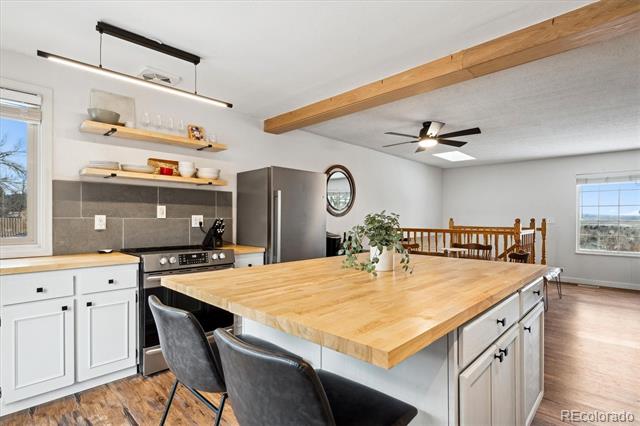 Kitchen with a large butcher-block island, white cabinetry, and an exposed wood ceiling beam.