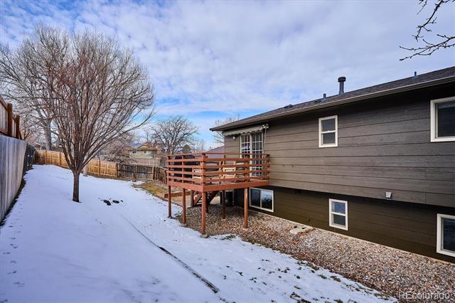 House exterior with a raised wooden deck overlooking a snow-covered, fenced backyard.