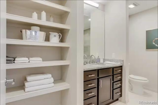 Bathroom with open towel shelves, a dark wood vanity, and a toilet.