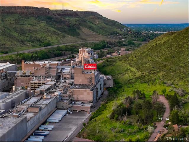 Aerial view of the Coors brewery, with green foothills and a winding hillside trail at sunset.