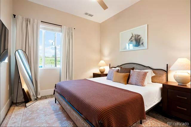 Furnished bedroom with a large bed, matching nightstands, and a full-length mirror beside the window.