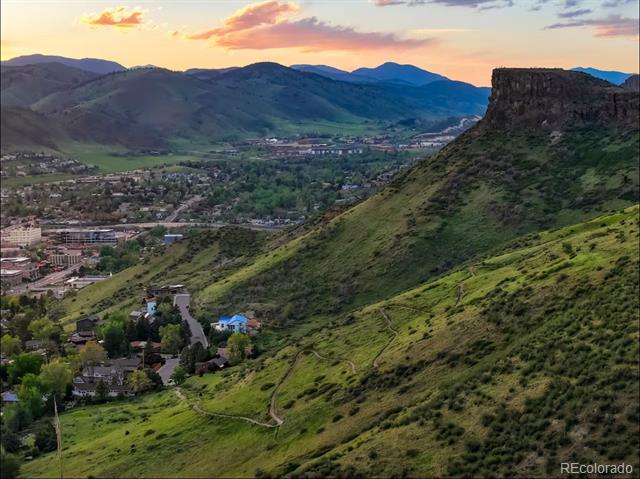 Mountain and town views at sunset, with a green hillside and prominent flat-topped mesa.