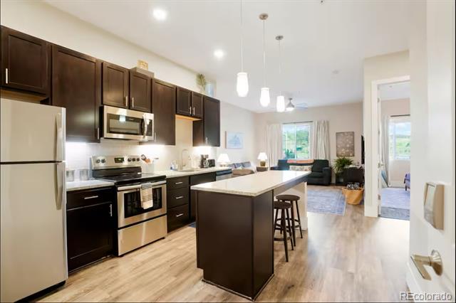 Open-concept condo kitchen with dark cabinets, stainless steel appliances, and a large island.