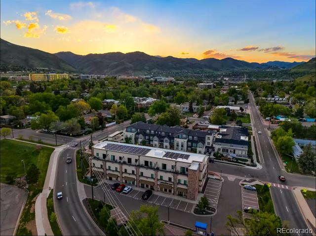 Aerial view of a residential building with rooftop solar panels, neighborhood streets, trees, and mountains at sunset.