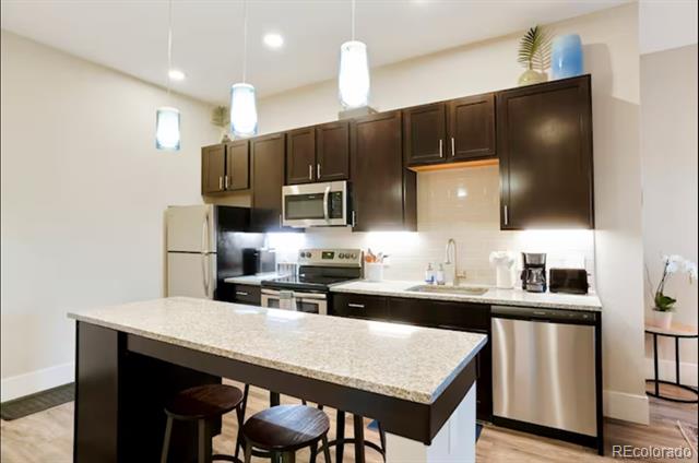 Kitchen with dark cabinets, stainless steel appliances, and a granite island with bar stools.