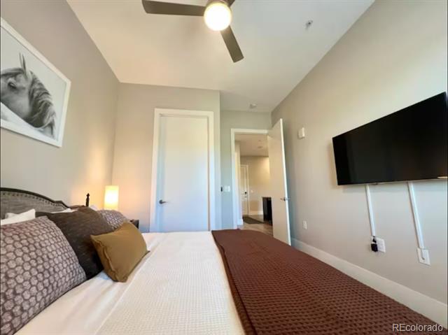 Bedroom with patterned bedding, a wall-mounted television, and a ceiling fan.