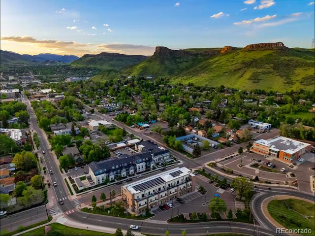 Aerial view of Golden neighborhoods and commercial buildings, backed by green foothills and a flat-topped mesa.