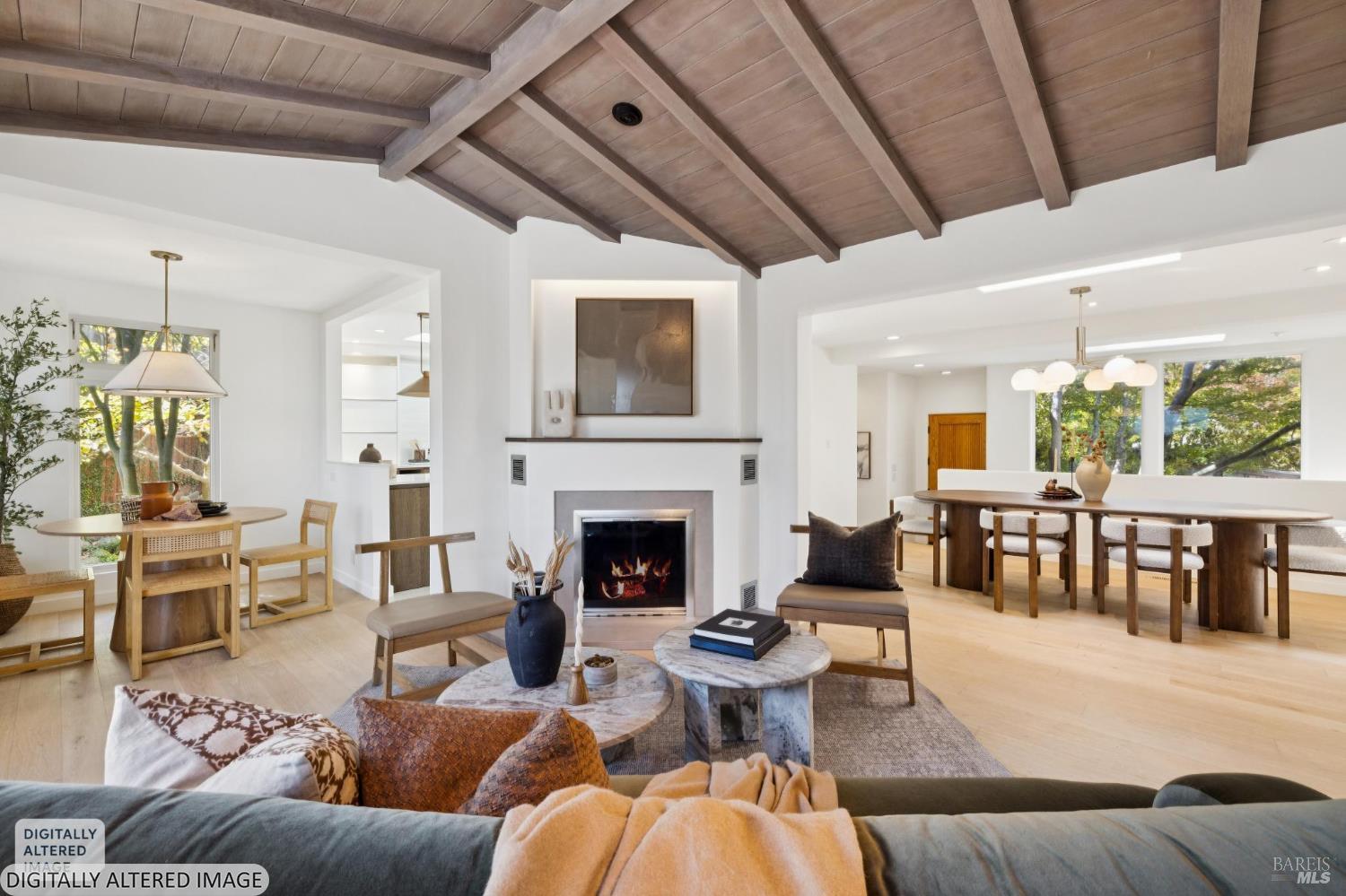 Open-plan living room with a fireplace, vaulted wood ceiling, and adjoining dining area.