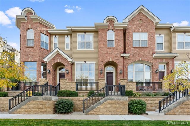 Connected brick and beige-sided townhomes with arched windows and stone retaining walls.
