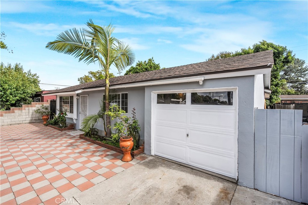 Single-story home with a white garage door, tiled driveway, and palm tree by the entrance.