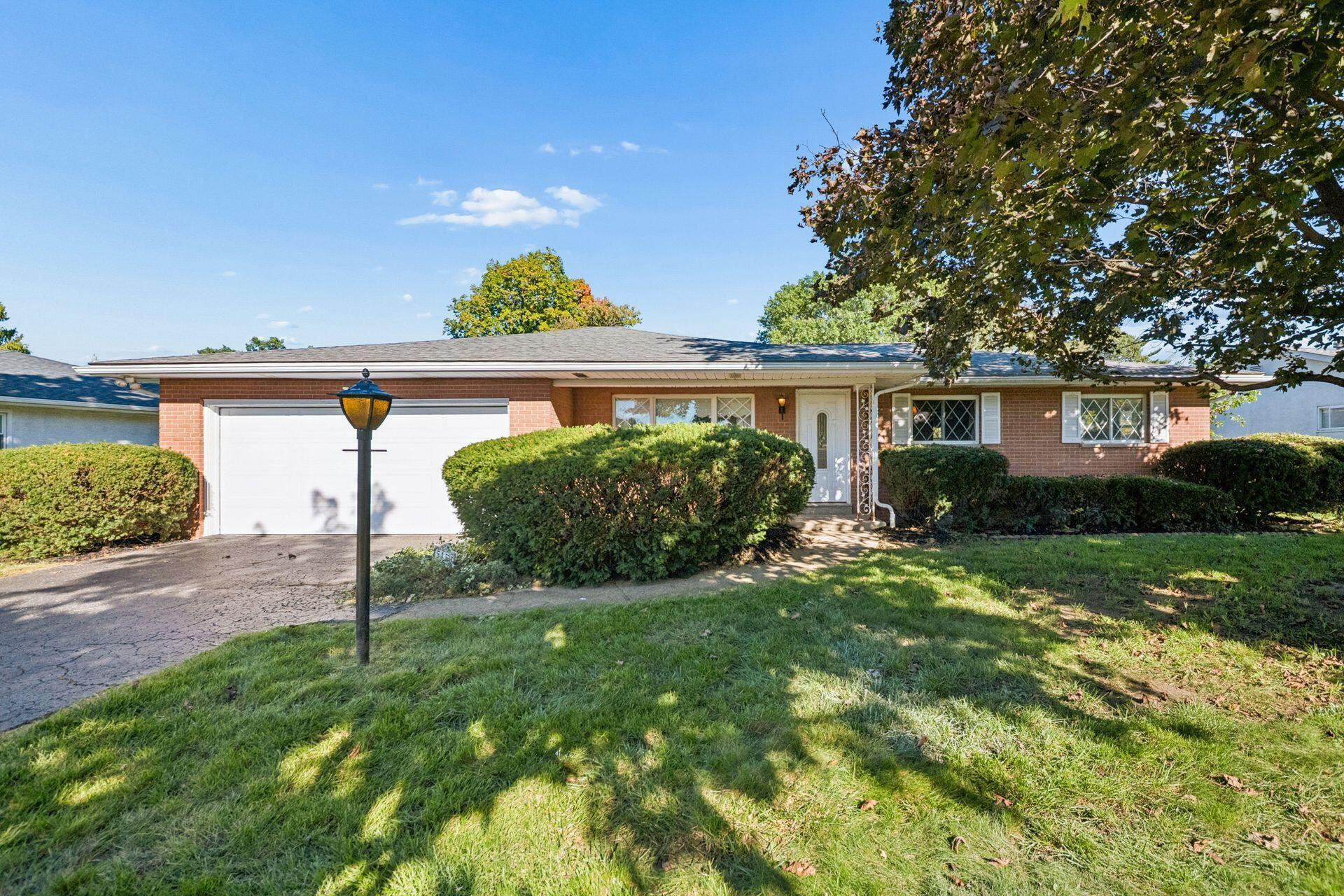 Single-story brick ranch house with a white garage door, diamond-pane windows, and a hedge-lined lawn.