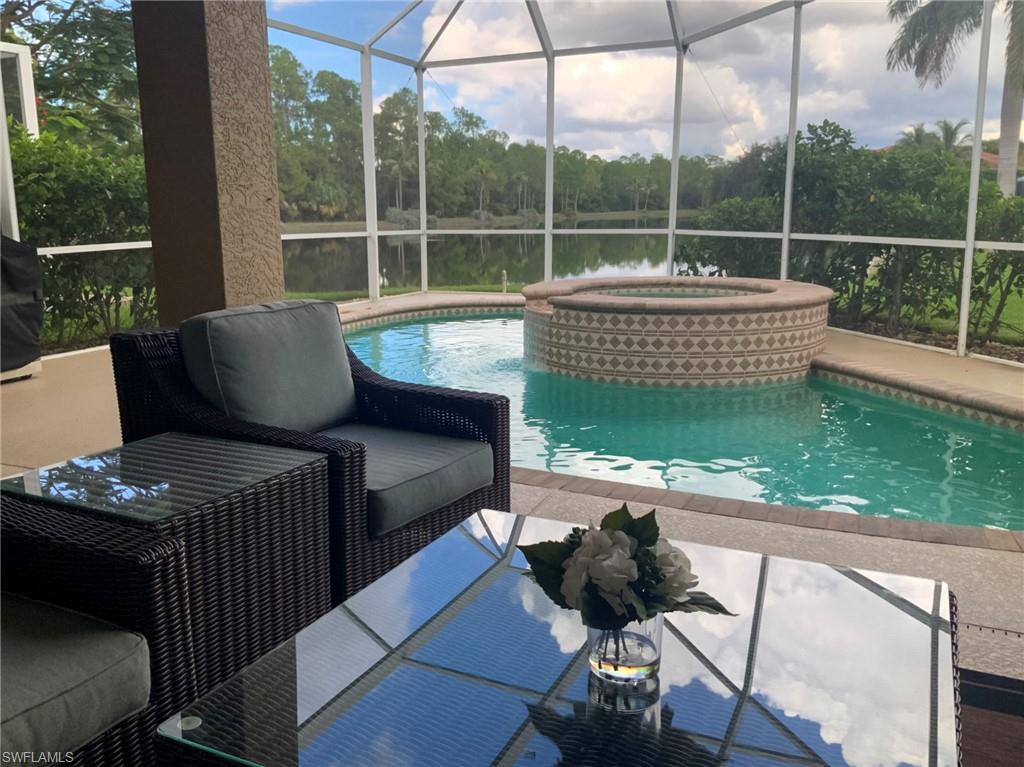 Screened lanai with a pool, raised circular spa, wicker seating, and lake view.