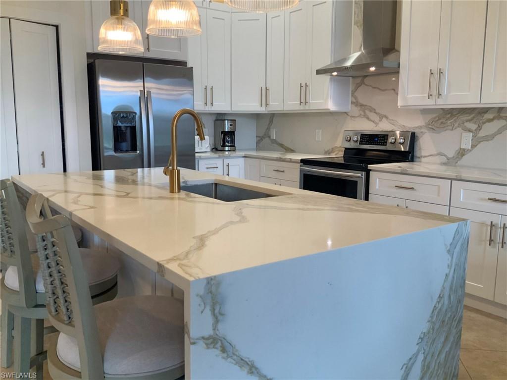 Modern kitchen with a marble-look waterfall island, gold-tone faucet, and white shaker cabinets.