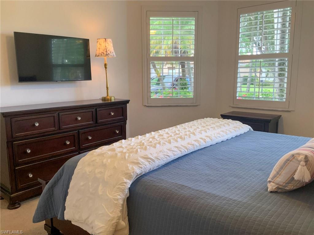 Furnished bedroom with a blue bedspread, dark wood dresser, and two shuttered windows.