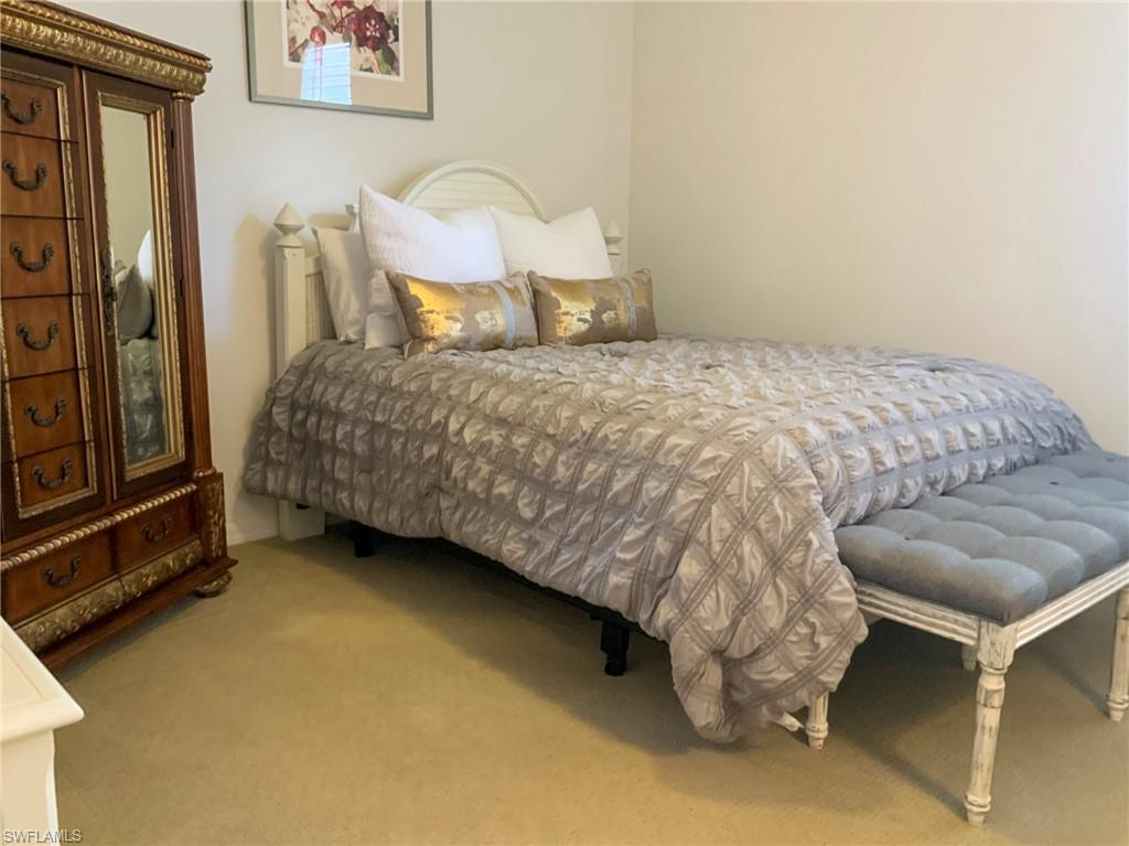 Furnished bedroom with a patterned bedspread, ornate wooden armoire, and tufted bench.