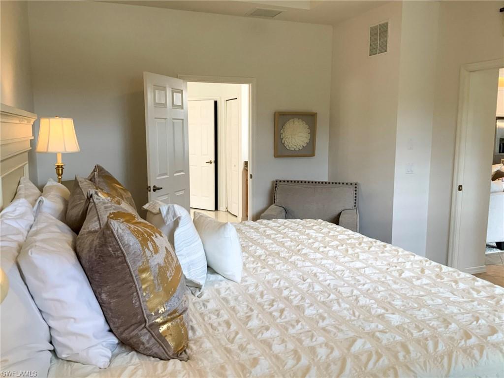 Bedroom with a white quilted bed, layered gold and taupe pillows, and a gray upholstered chair.