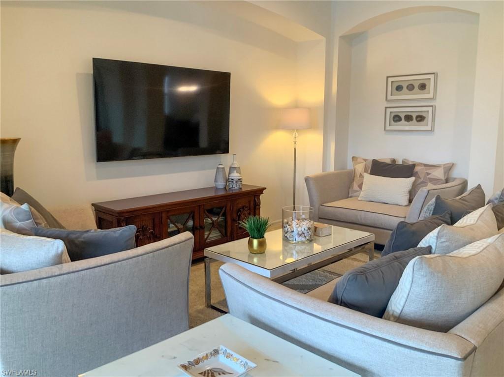 Furnished living room with neutral seating, a glass coffee table, and a wall-mounted television.