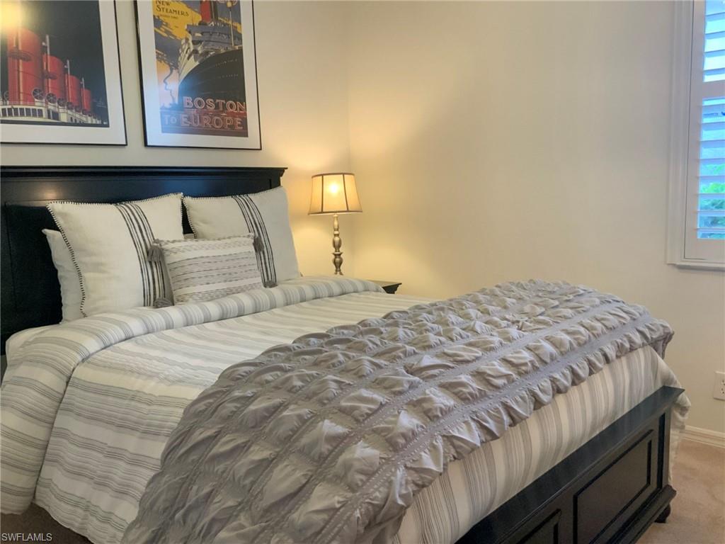 Bedroom with striped bedding, a dark wood bed, framed travel posters, and a shuttered window.