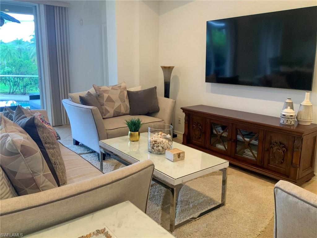 Living room with beige sofas, a marble-top coffee table, and a large wall-mounted television.