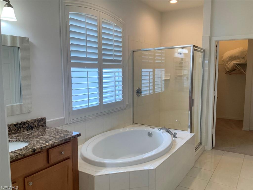 Bathroom with an oval soaking tub, glass shower, plantation shutters, and granite vanity.