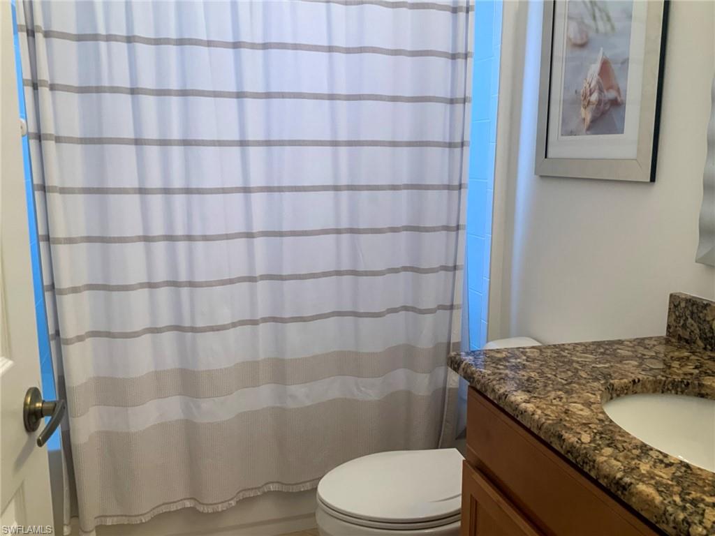 Bathroom with a striped shower curtain, white toilet, and granite vanity.