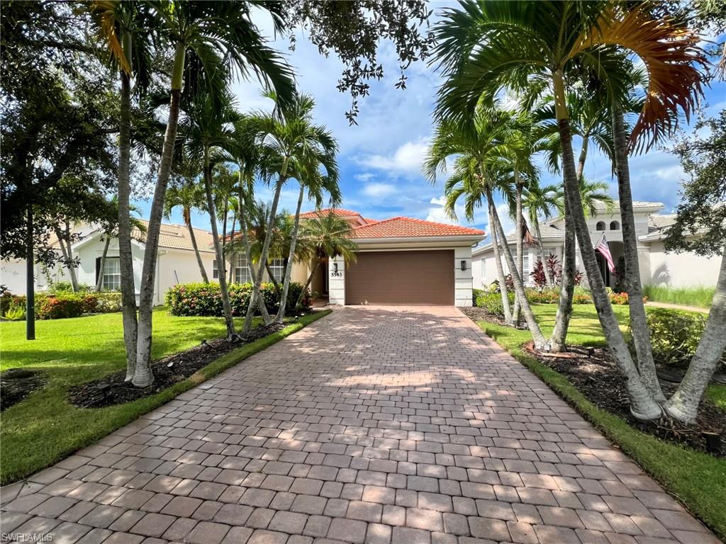Home with a red tile roof and paver driveway, framed by palm trees.