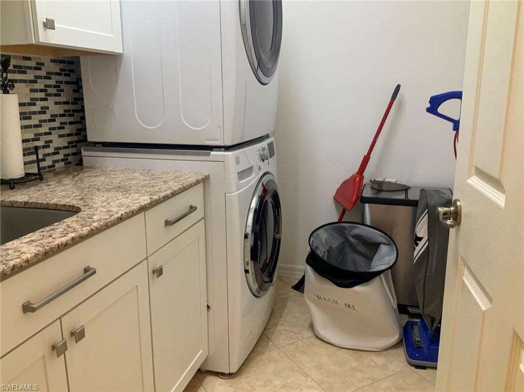 Laundry room with stacked washer and dryer, granite counter, sink, and mosaic tile backsplash.