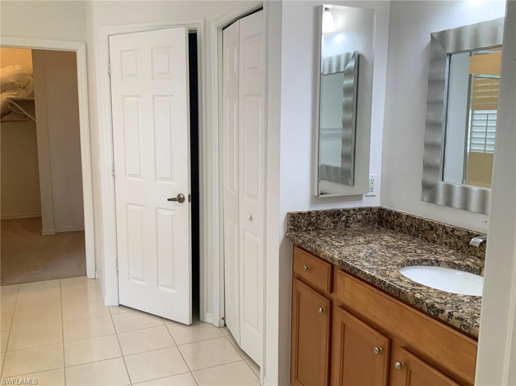 Bathroom vanity with wood cabinets, granite countertop, two mirrors, and an open doorway to a carpeted room.
