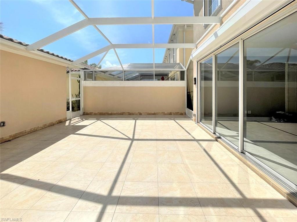 Unfurnished tiled patio beneath a screened enclosure, with sliding glass doors along the house.