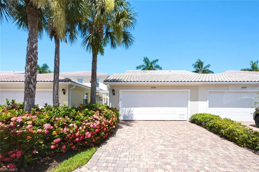 Home exterior with a paver driveway, flowering shrubs, palm trees, and garage marked 8090.