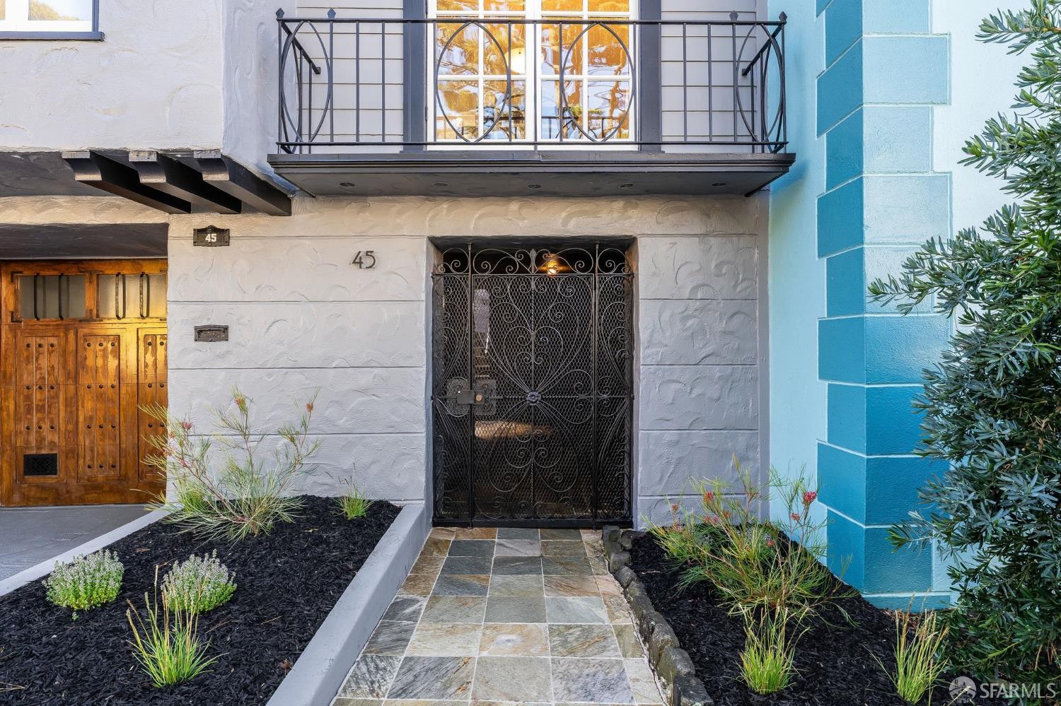 Home entrance with an ornate iron gate, stone walkway, and balcony above.